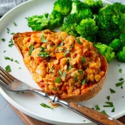 Lentil stew-stuffed sweet potatoes on a white plate with steamed broccoli.