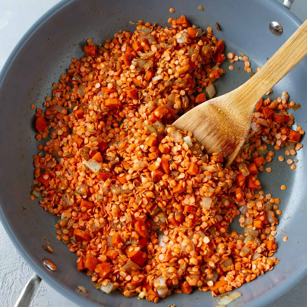 Red lentils, sautéed vegetables and a wooden spatula in a skillet.