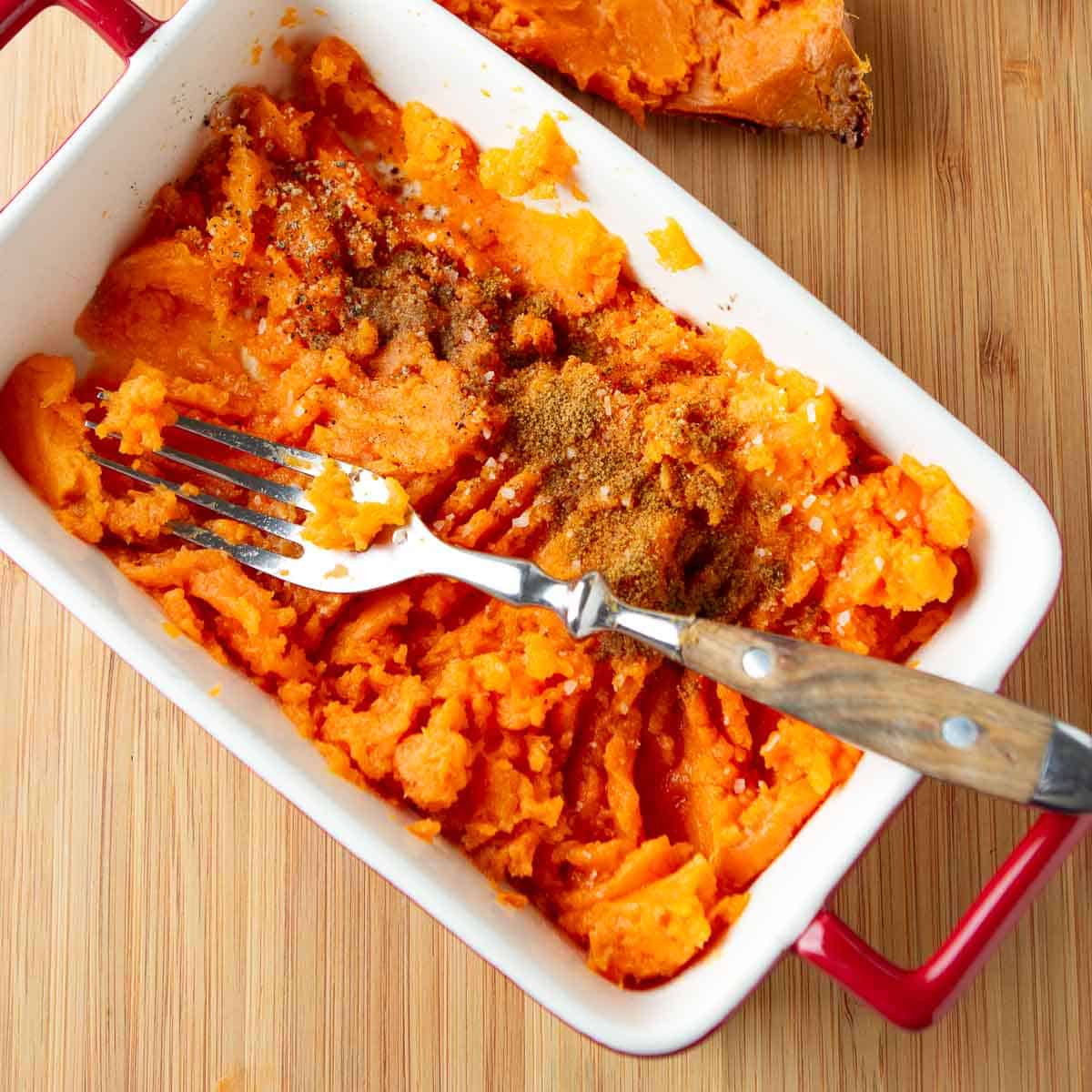 Smashed sweet potatoes with cinnamon and a fork in a small baking dish.