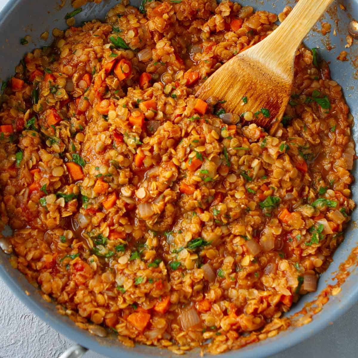 Cooked lentil stew and wooden spatula in a skillet.