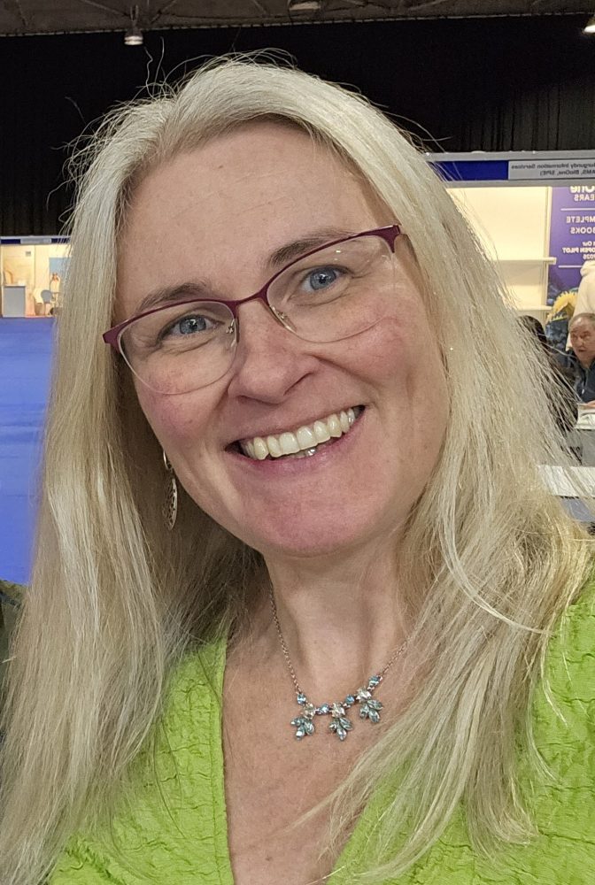 Sian, a white women with long, straight blonde hair and glasses, smiles at the camera.