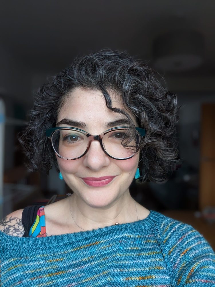 Tasha, a white woman with dark curly hair, stares at the camera.