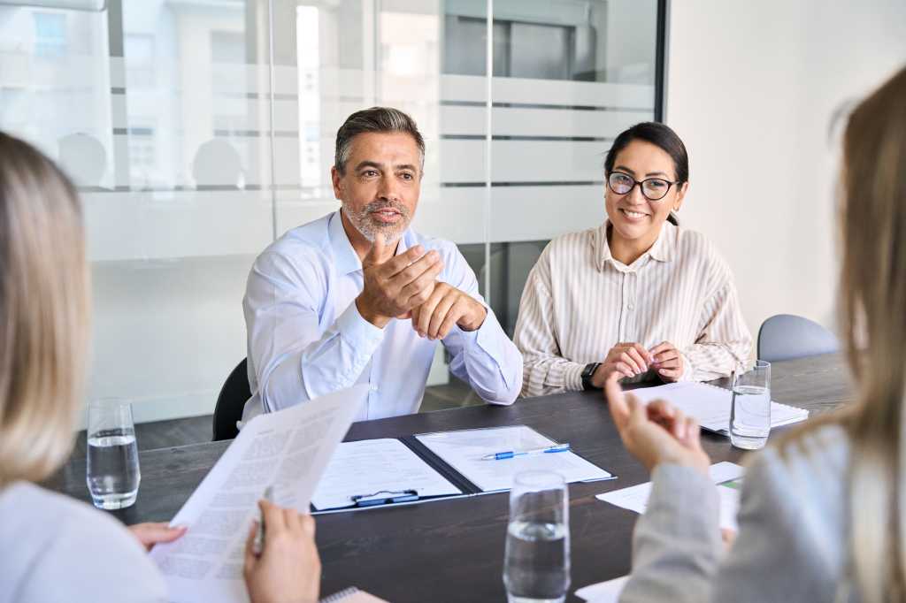 Diverse professional executive team working at meeting in office. Mid aged business man manager leader talking to board people consulting partners investors discussing project management in teamwork.