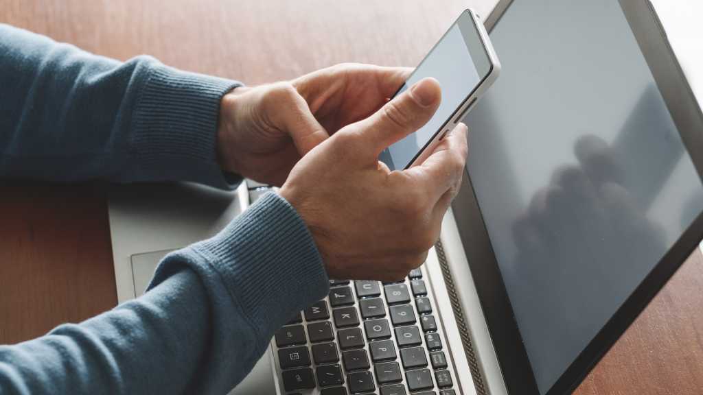 Person holding phone near a laptop while getting two-factor authentication info