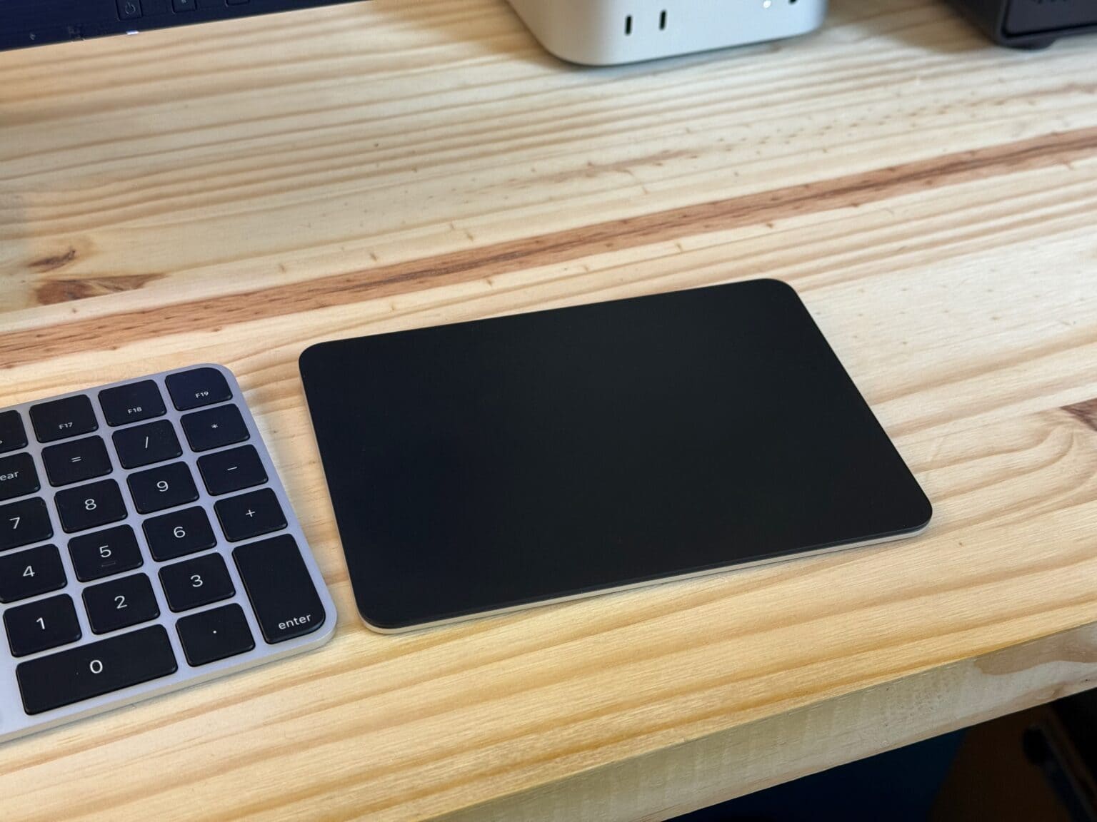 Black Magic Trackpad sitting on a desk next to a black Magic Keyboard and Mac mini.