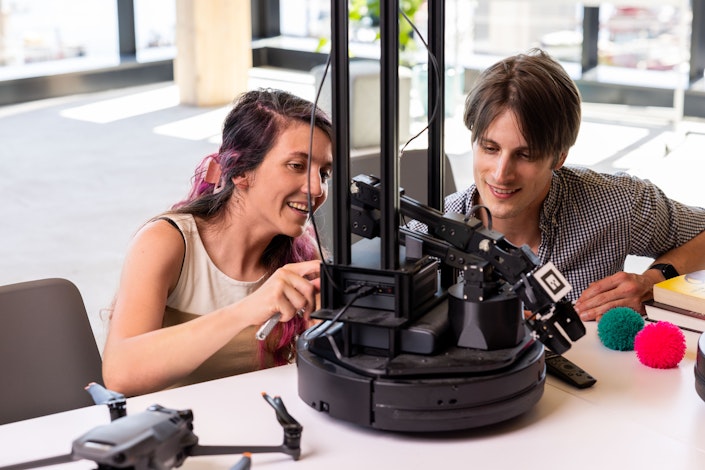 Two Ai2 team members working together on a locobot robot sitting on a while table.