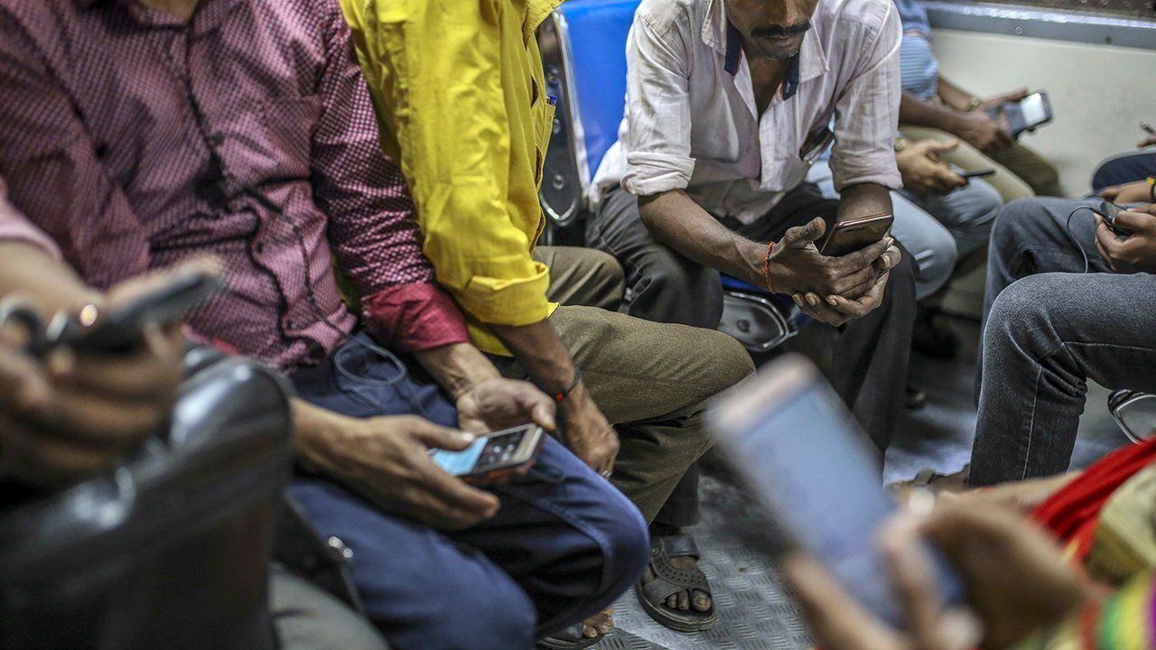 Passengers use smartphones while riding on a train in Mumbai