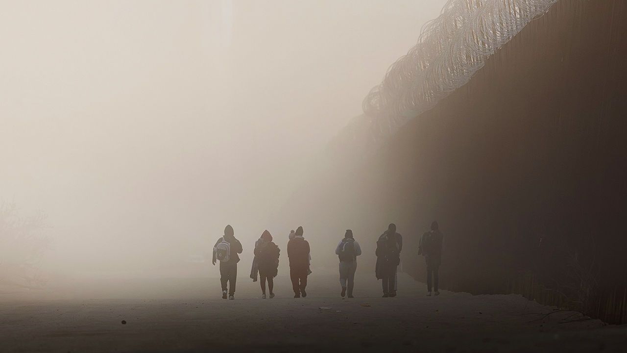  Asylum-seeking migrants walk along the US-Mexico border fence near the Jacumba Hot Spring, California