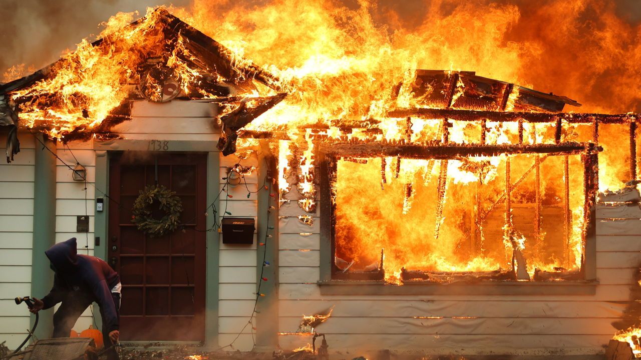 A person turns on a garden hose in an effort to save a neighboring home from catching fire during the Eaton Fire in Altadena, California, USA.