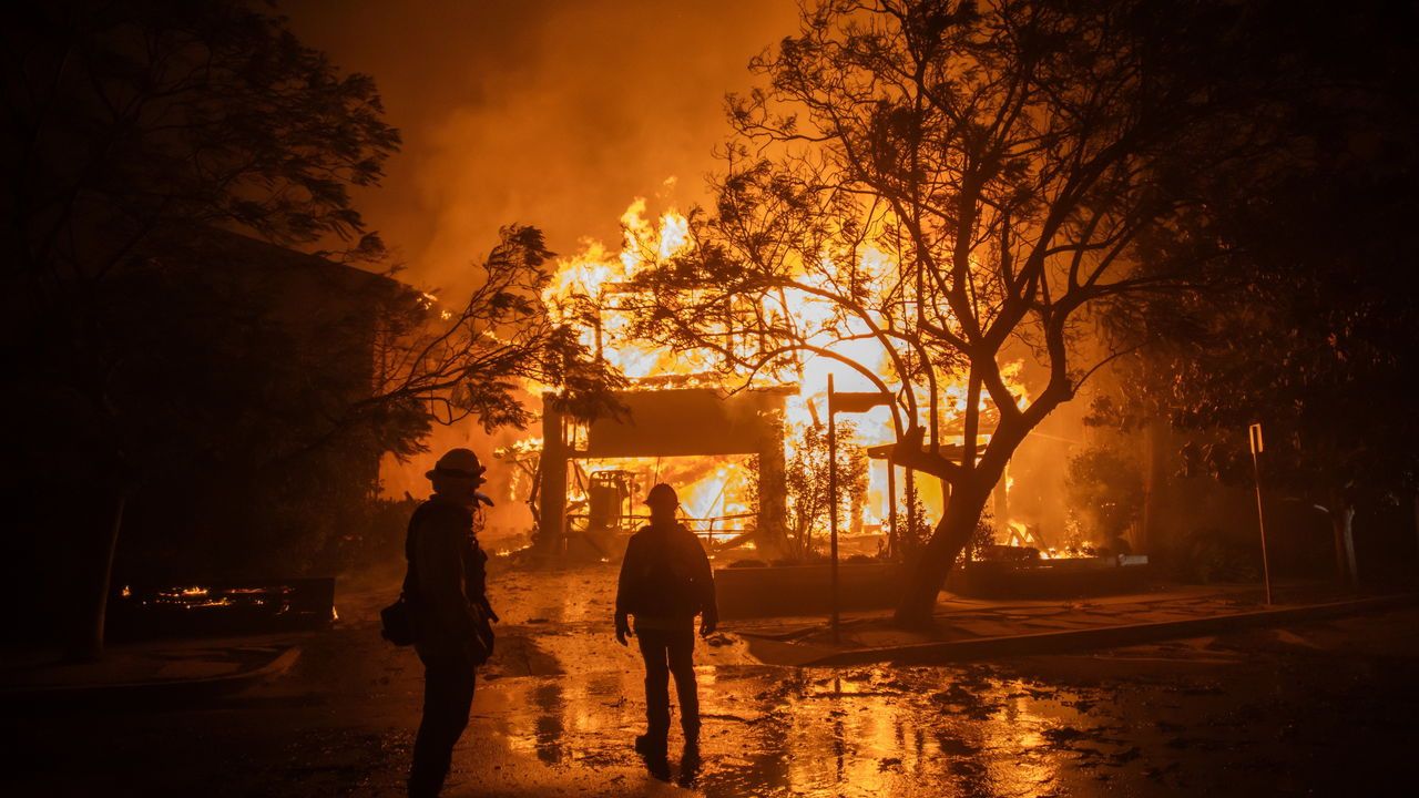 Firefighters watch flames burning a home in Palisades, Los Angeles, California