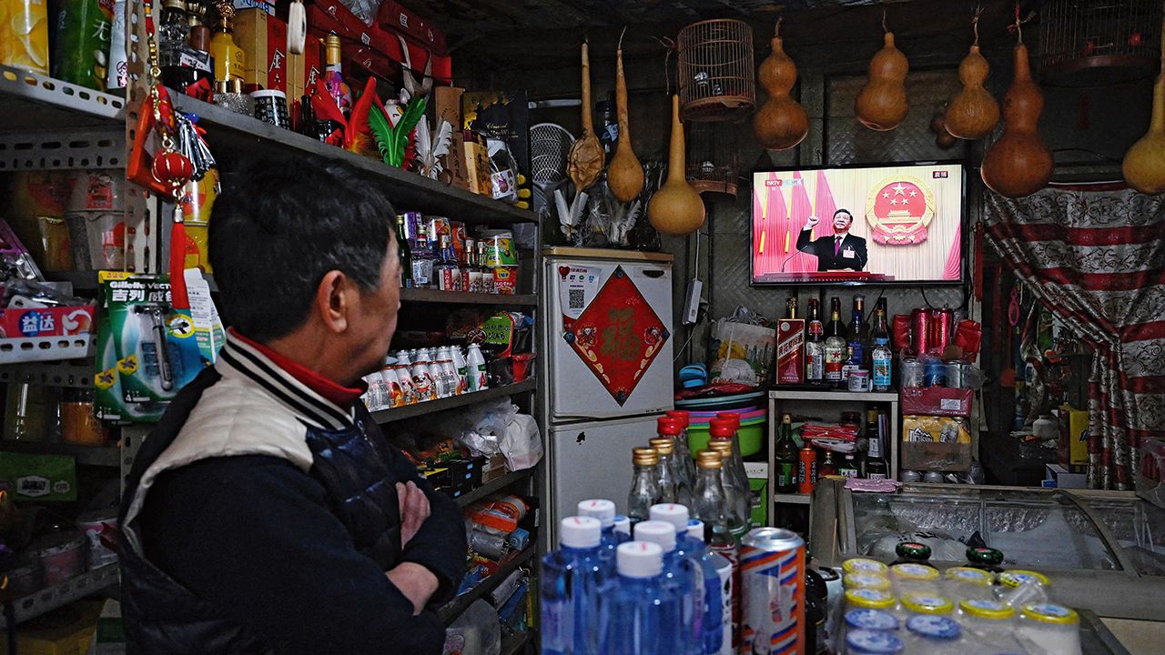 A man watches live coverage on a TV screen at his store of Chinese President Xi Jinping 