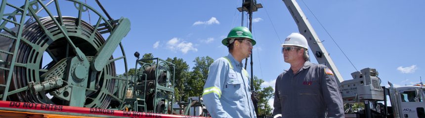 Two people talking with a crane and flat bed truck in the background. 