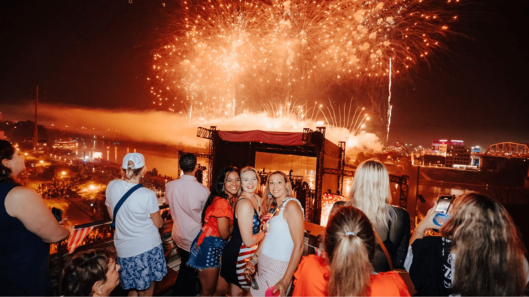 Attendees smile and pose in front of fireworks