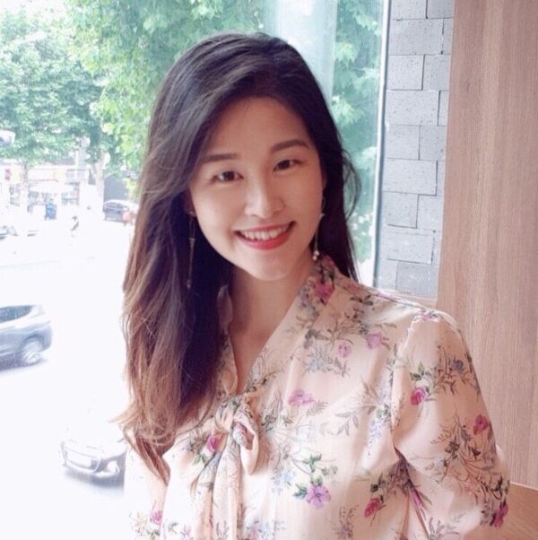 Yoonsu Cho, smiling in front of a window, trees in the background.