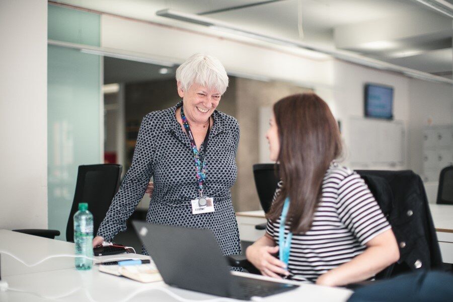 Older female approaching and smiling at younger female in office