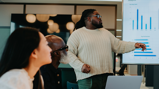 A photo of people in a meeting discussing analytics that are being displayed in a dashboard. 