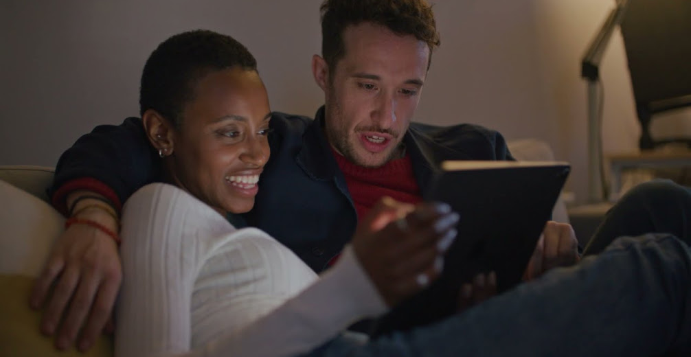 A couple watches media on their tablet while sitting on a sofa.