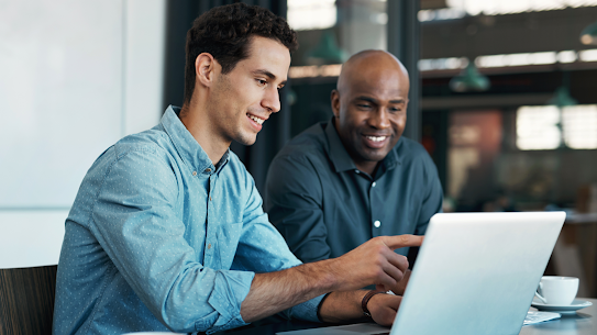 A photo of two professionals engaged in a discussion while working on a laptop.