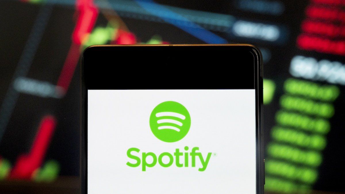 In this photo illustration, the Swedish music streaming platform Spotify (NYSE: SPOT) logo seen displayed on a smartphone with an economic stock exchange index graph in the background.