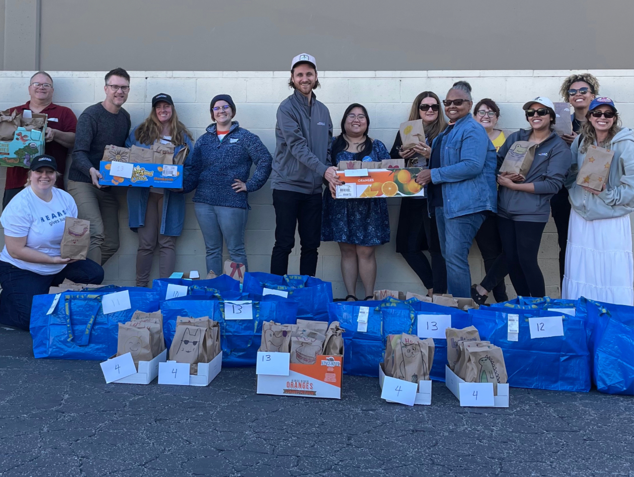 Group of 13 people smiles for camera while holding boxes with bags at their feet