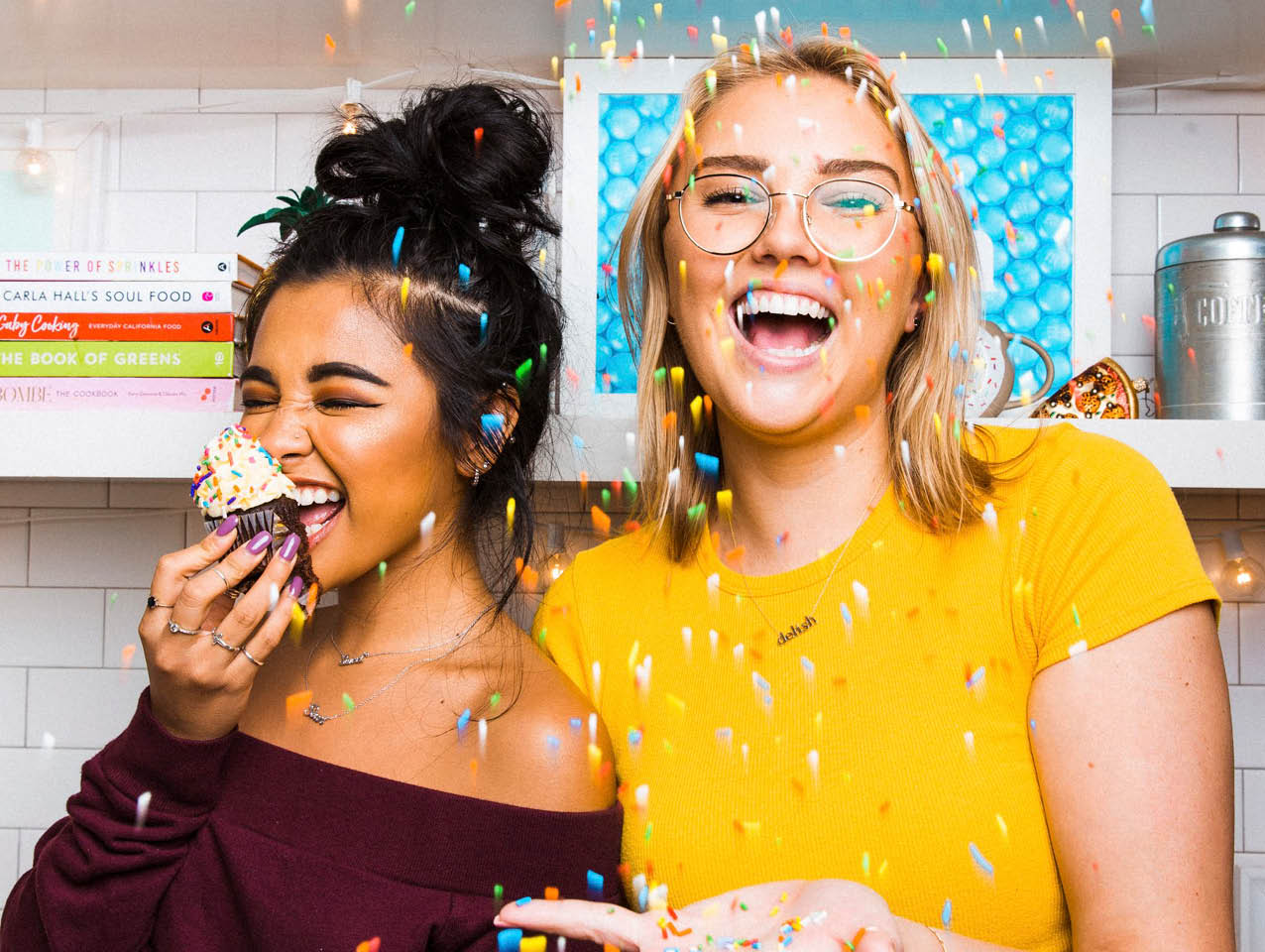 smiling colleagues in Delish kitchen eating cupcakes with confetti falling