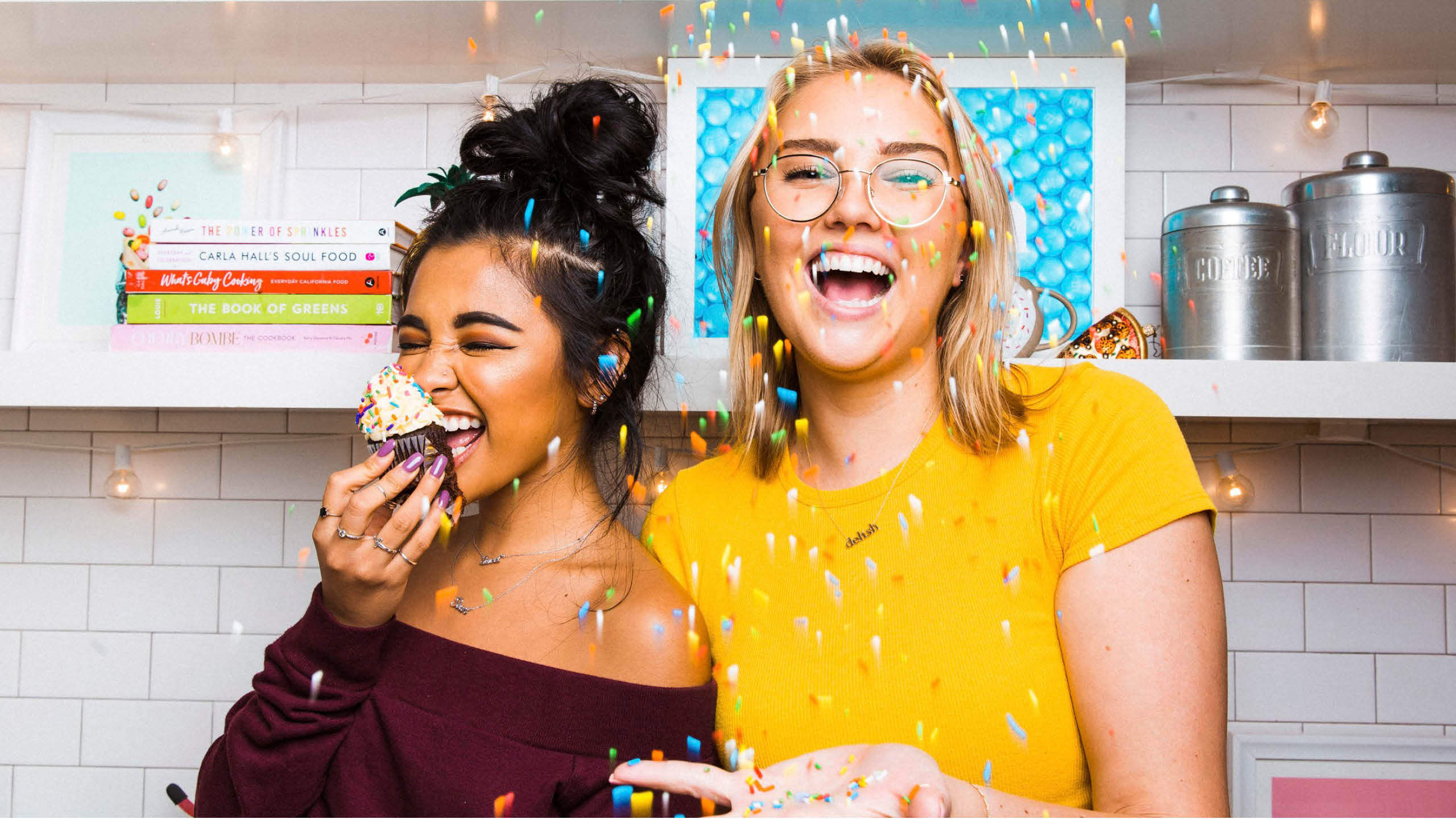 two colleagues in the delish kitchen eating cupcakes with confetti falling