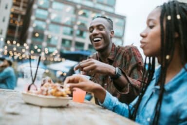 A couple dining at an outdoor table, sharing food and laughter, demonstrating how they've applied dating tips for finding the right person.