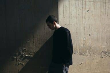 A man leans against a stark concrete wall, implying the challenges of knowing how to help someone with bipolar disorder