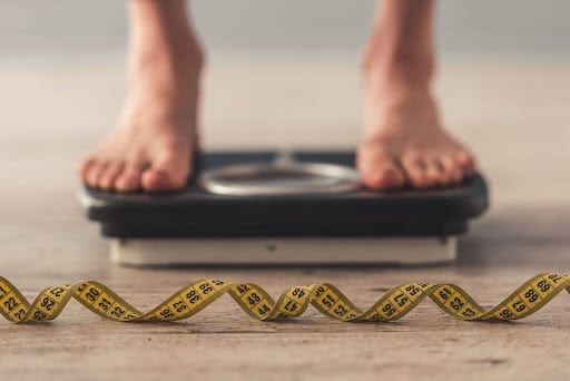 Feet standing on a scale with a tape measure on the ground in front of it