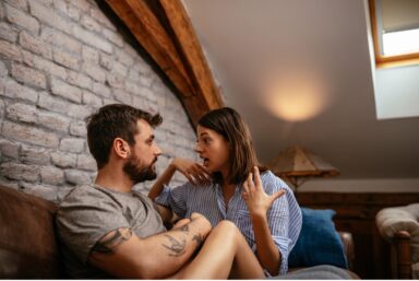 A man is actively listening to a woman talking, while they’re seated comfortably on a couch in a cozy living room setting.