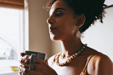 A woman relaxes by the window, sipping coffee, as natural light illuminates her serene moment enjoying caffeine.