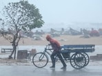 A man pulls his three-wheeler cart amid heavy wind and rainfall at the Marina Beach in Chennai.(AFP)