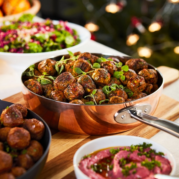 A pan full with veggie balls cooked, placed on a wooden chopping board on a dining table.