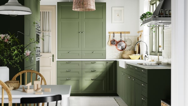 A kitchen with AXSTAD grey-green fronts, brightened by natural light, complemented by white tiles and wooden accents.