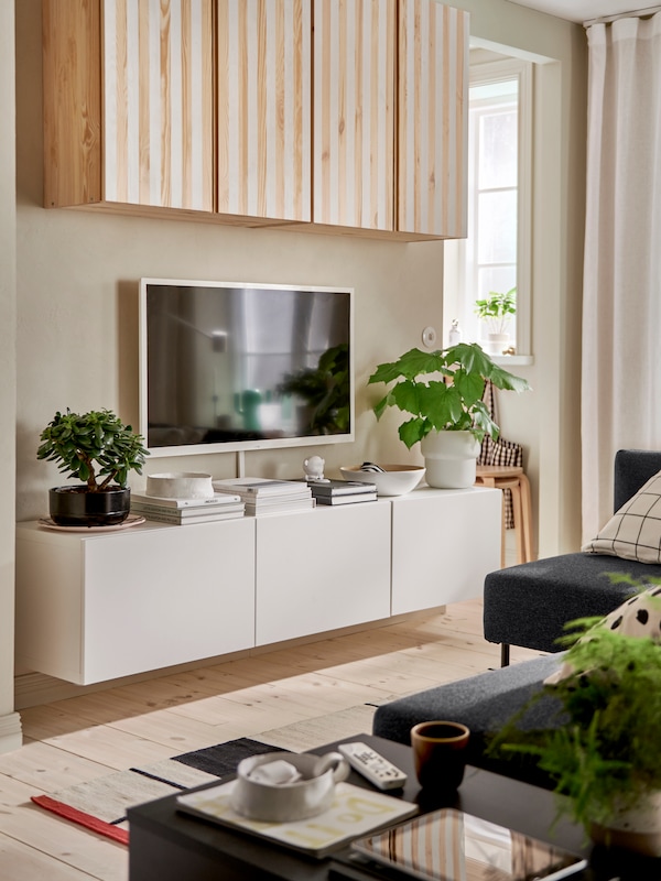 A white BESTÅ TV bench with doors is mounted on a wall underneath a wall-mounted TV and IVAR cabinets painted with stripes.