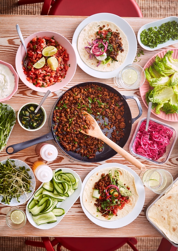 A frying pan with taco mince made from HUVUDROLL plant-balls minced next to plates and bowls with Pico de Gallo and tortillas.