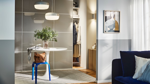 IKEA SKYTTA sliding doors attached to a wardrobe white frame in a sunny bedroom, a white round table with a plant on top and a dark blue sofa in the corner.