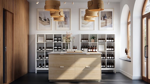 A bright, spacious store interior centred round a large kitchen island with light-ash-effect ASKERSUND drawer fronts.