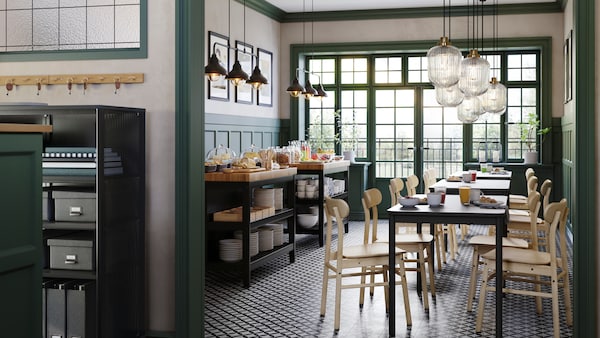 A café with green wall panels and TOMMARYD tables, birch RÖNNINGE chairs and two VADHOLMA kitchen islands.