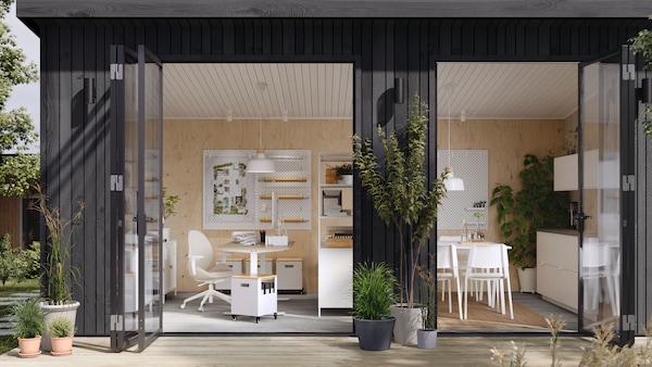 A garden studio with open doors showing a desk and chair work area, open shelving divider and a communal kitchen area.