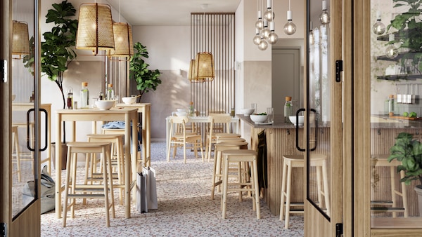 A light, airy restaurant with tidily arranged RÖNNINGE birch bar tables and bar stools under KNIXHULT bamboo pendant lamps.