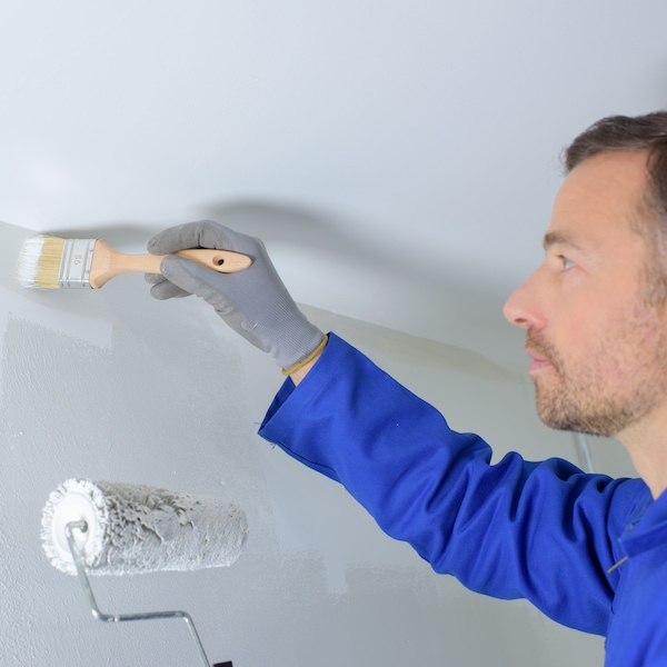 A man wearing a bright blue shirt painting a wall with white paint.