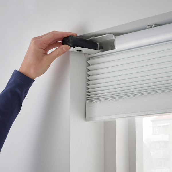 A person installing a white blind onto a window.