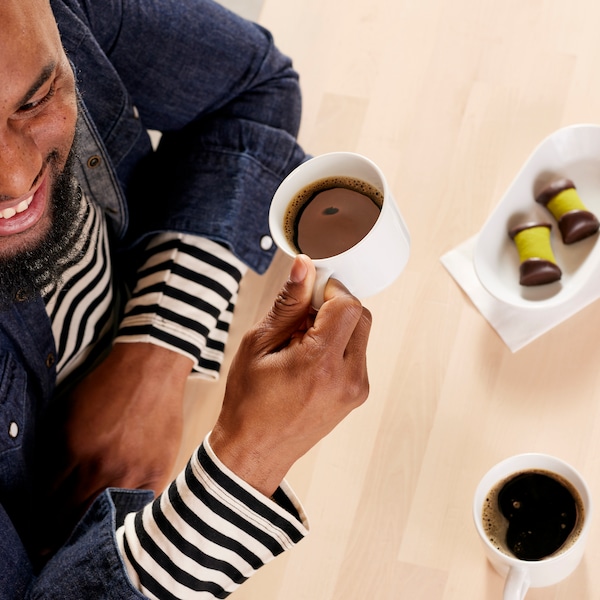 A person wearing a blue denim shirt and stripped top drinking black coffee in white mugs.