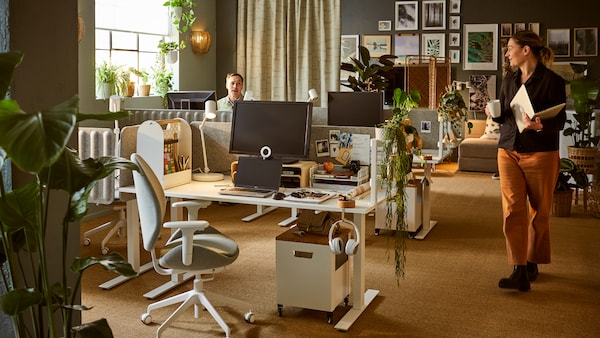 A softly sunlit office interior with several workspaces, surrounded by plenty of leafy plants, decorations and wall art.