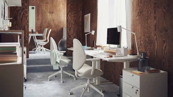 Workspaces with white TROTTEN desks and HATTEFJÄLL and LÅNGFJÄLL office chairs in a carpeted, brown, wood-panel office.