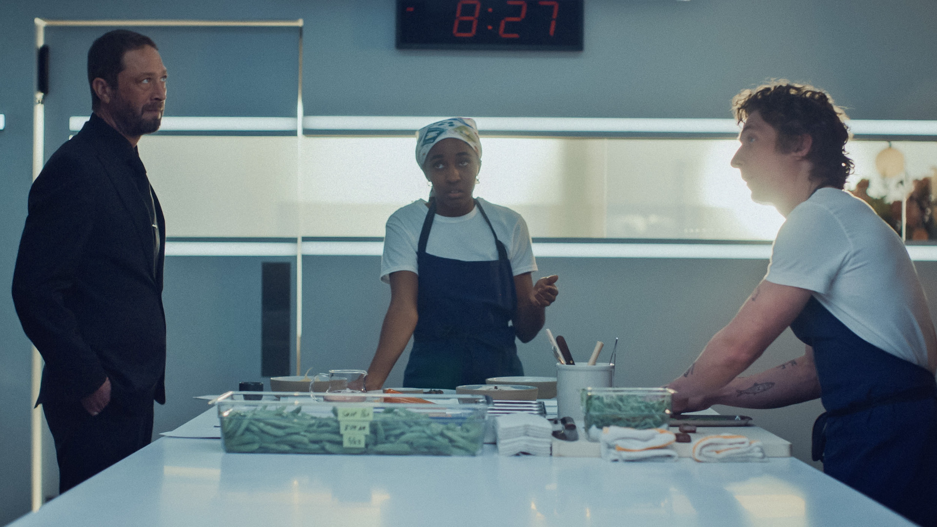 Two chefs and a host gathered around a white counter with food prep; still from 'The Bear'