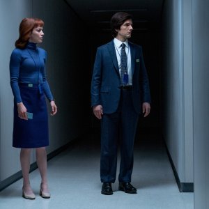 A woman in blue and a man wearing a dark suit walking in a dark white-walled hallway; still from 'Severance' Season 2