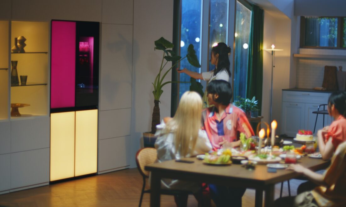 A woman is remotely playing music via a built-in Bluetooth speaker of the LG MoodUPTM refrigerator at the house party