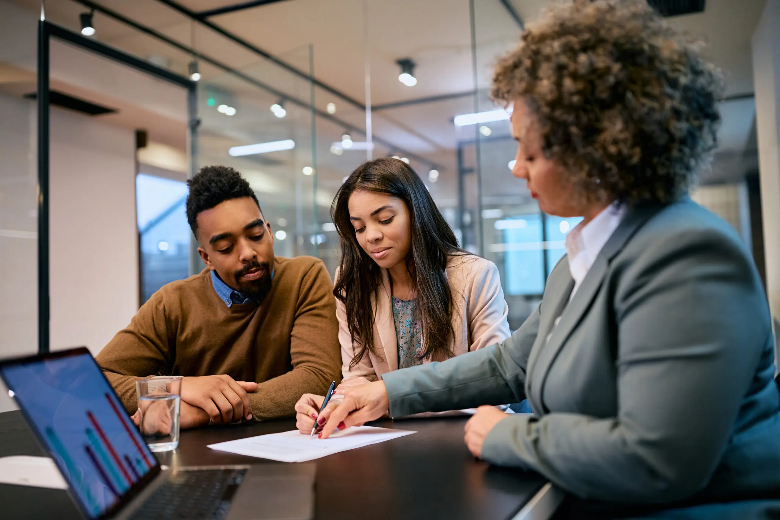 African American woman and her husband signing mortgage agreement during a meeting with their bank manager.